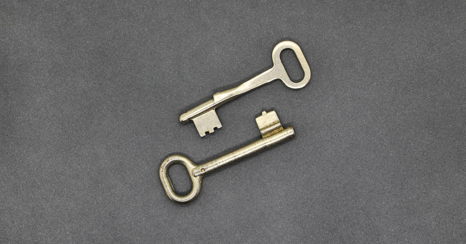 Two near-identical brass keys lying side by side on a dark grey surface