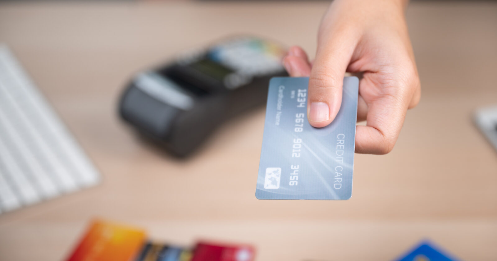 A hand holding a credit card over a payment terminal, with more cards fanned out below