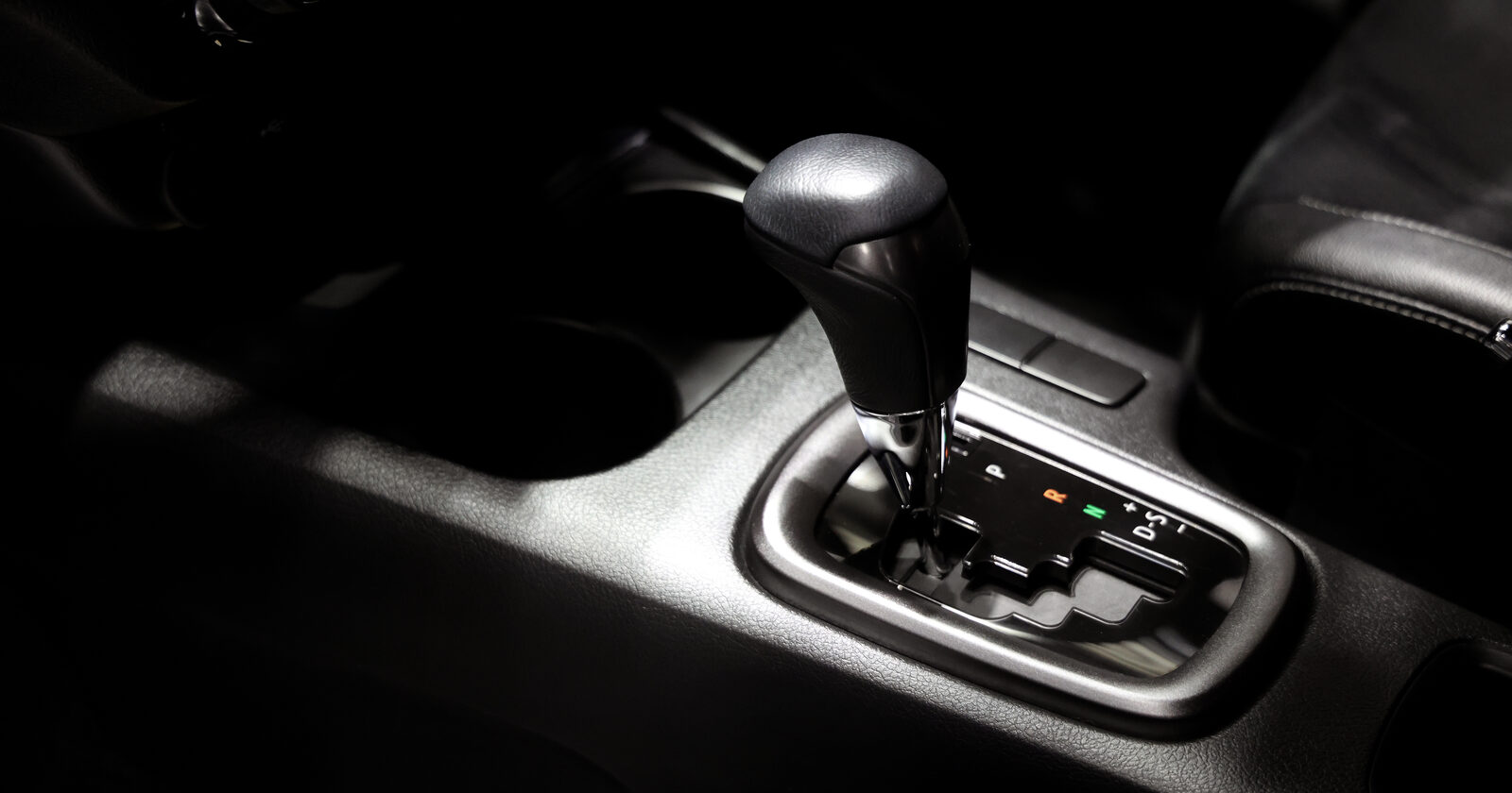 A black automatic gear selector lit against a dark car interior, the P R N D gate visible beside it